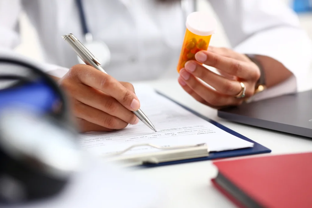 Doctor holding a jar of pills while writing a prescription
