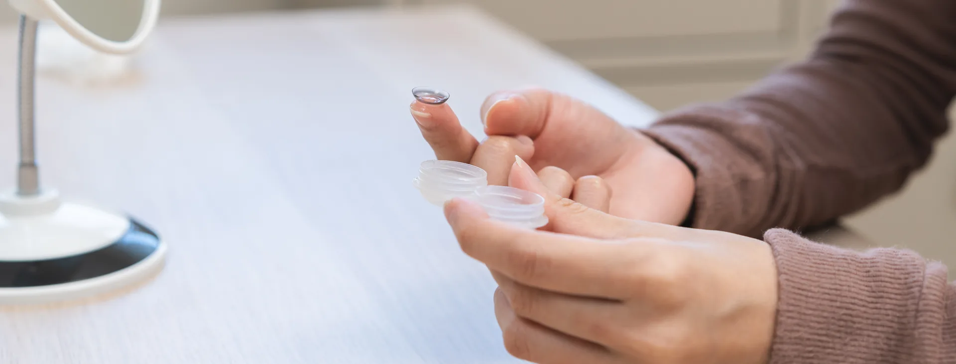 Person holding a contact lens on a fingertip beside a lens case