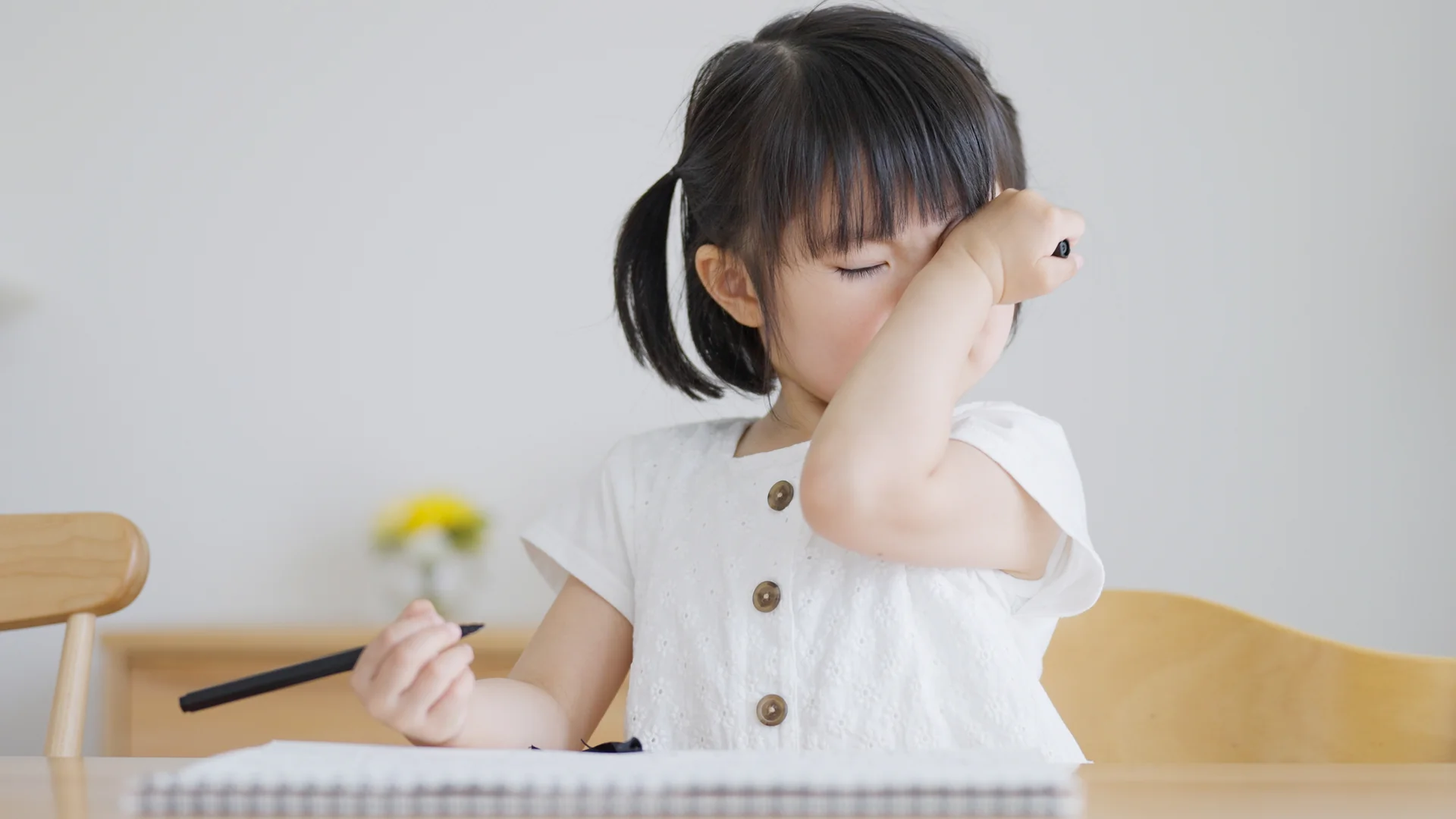 Young girl rubbing her eye while drawing at a table