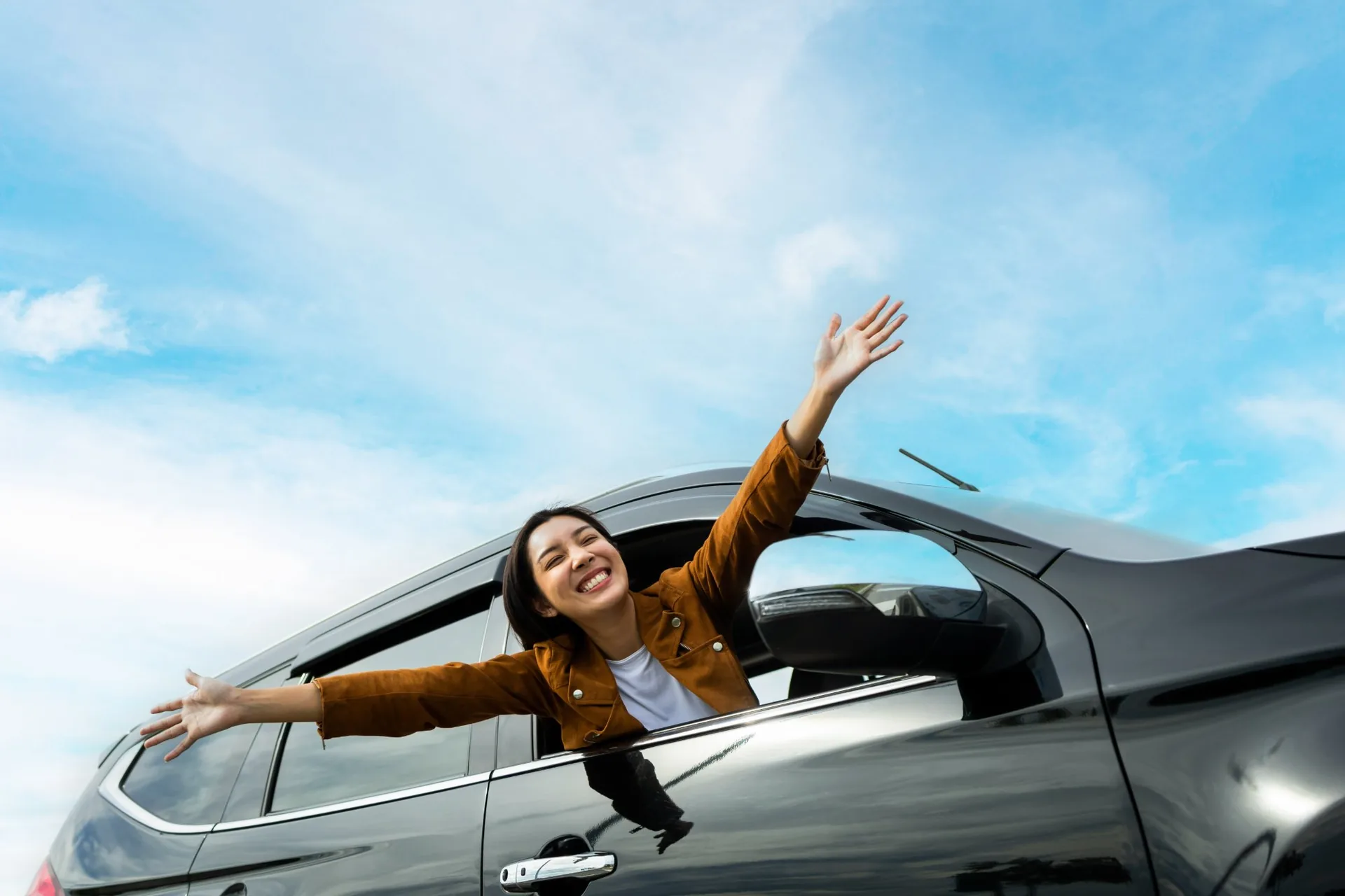 Woman waving happily from a car window enjoying clear vision