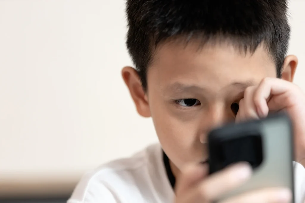 Boy rubbing his eye while looking at a phone