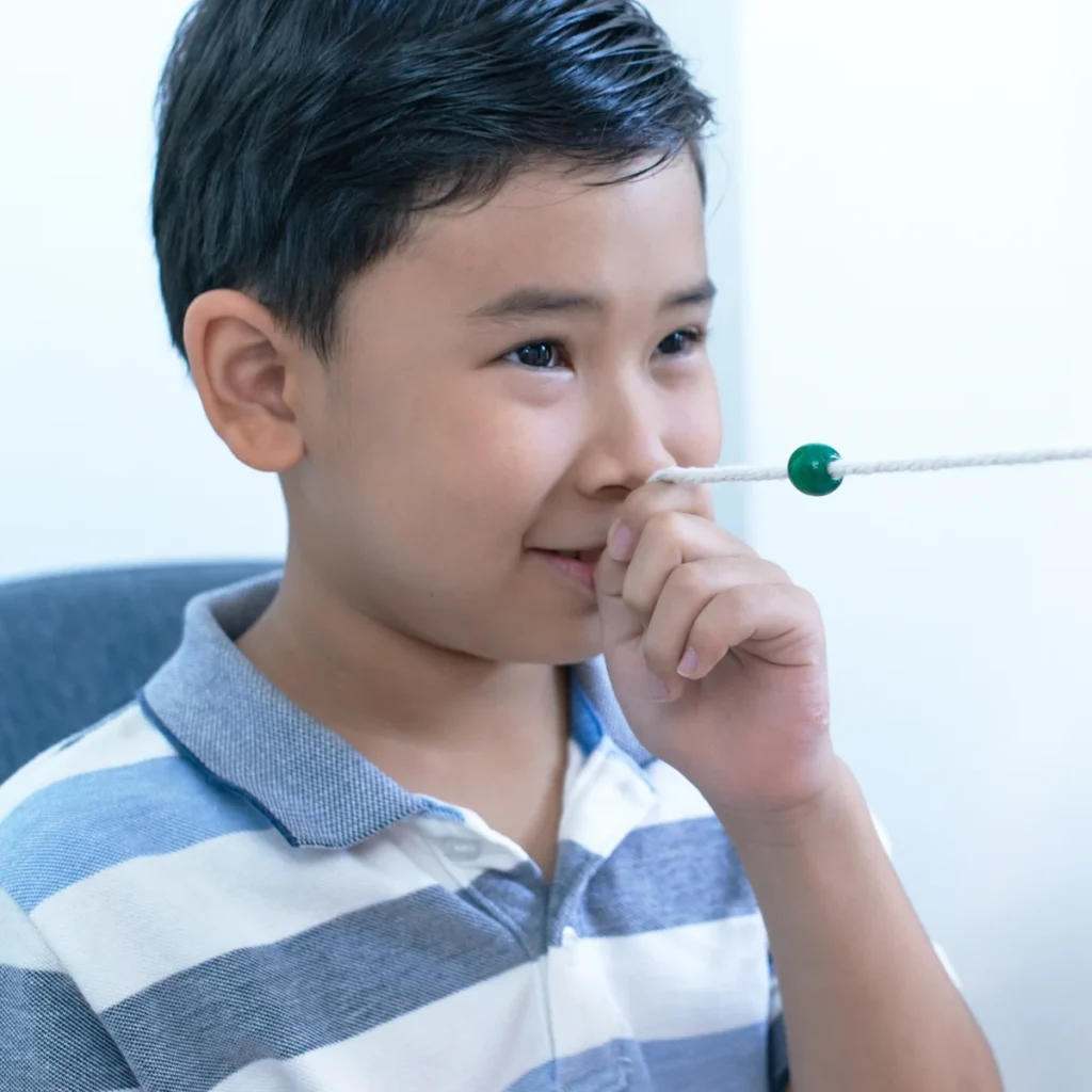 Boy doing an eye exercise with a bead string held to his nose